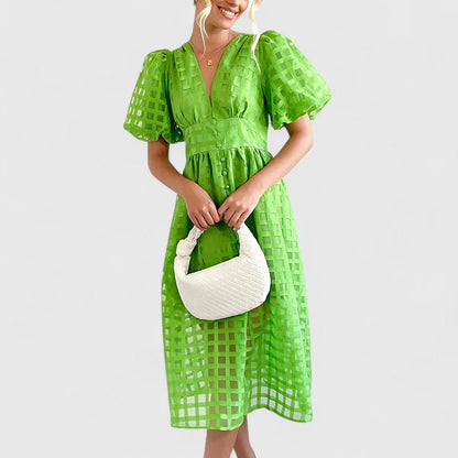 Green - A woman wearing a black grid organza midi dress with puff sleeves, a deep V-neck, and a button-front bodice, holding a woven beige handbag.