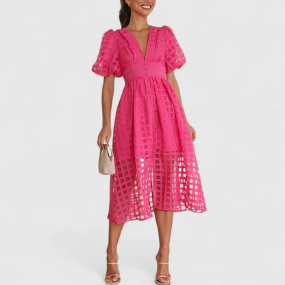 Pink - A woman wearing a black grid organza midi dress with puff sleeves, a deep V-neck, and a button-front bodice, holding a woven beige handbag.