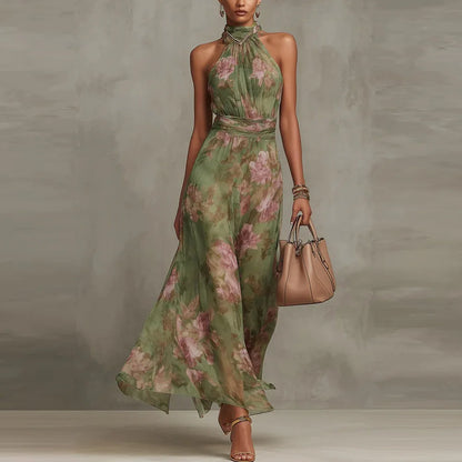 Green - A woman wearing a sage green and dusty pink watercolor floral print chiffon maxi dress with a high halter neck, ruched waist, and flowy floor-length skirt.