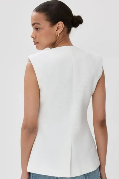 Woman wearing white boucle vest with tortoise buttons