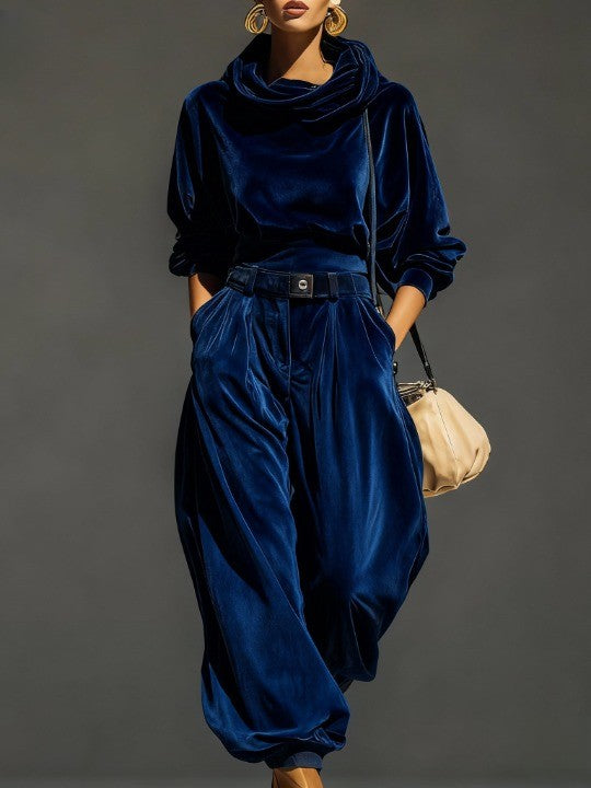 Woman wearing brown velvet cowl neck top and wide leg pants with cream-colored purse.