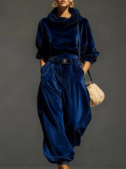Woman wearing brown velvet cowl neck top and wide leg pants with cream-colored purse.