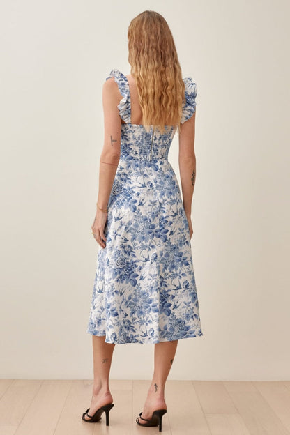 Woman wearing blue and white floral linen midi dress with ruffle straps and thigh slit