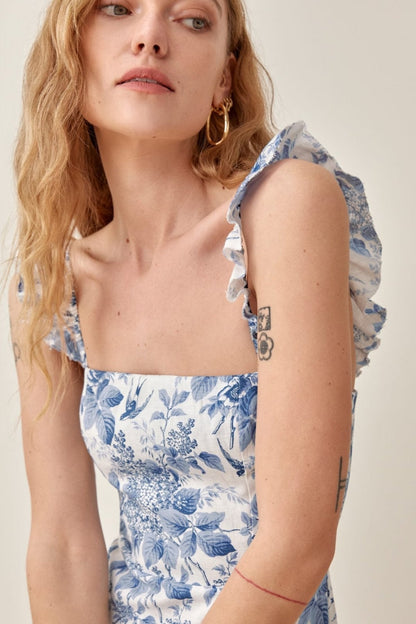 Woman wearing blue and white floral linen midi dress with ruffle straps and thigh slit