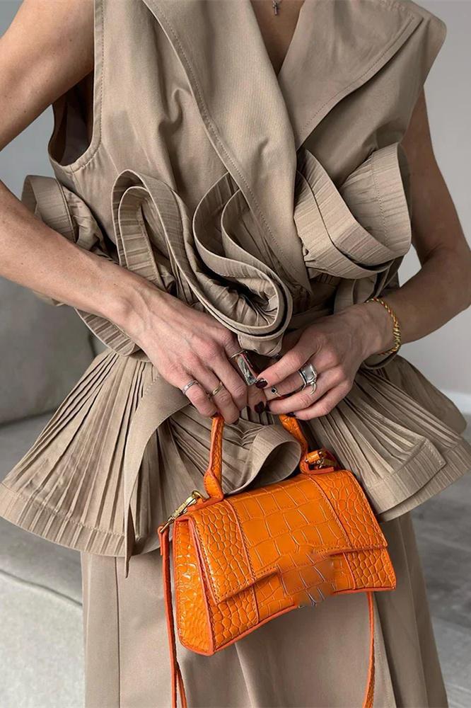 Woman wearing tan sleeveless trench vest with orange purse