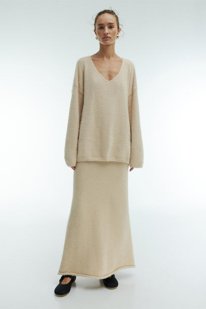 Woman in off-white boucle knit sweater and maxi skirt set with fuzzy slippers