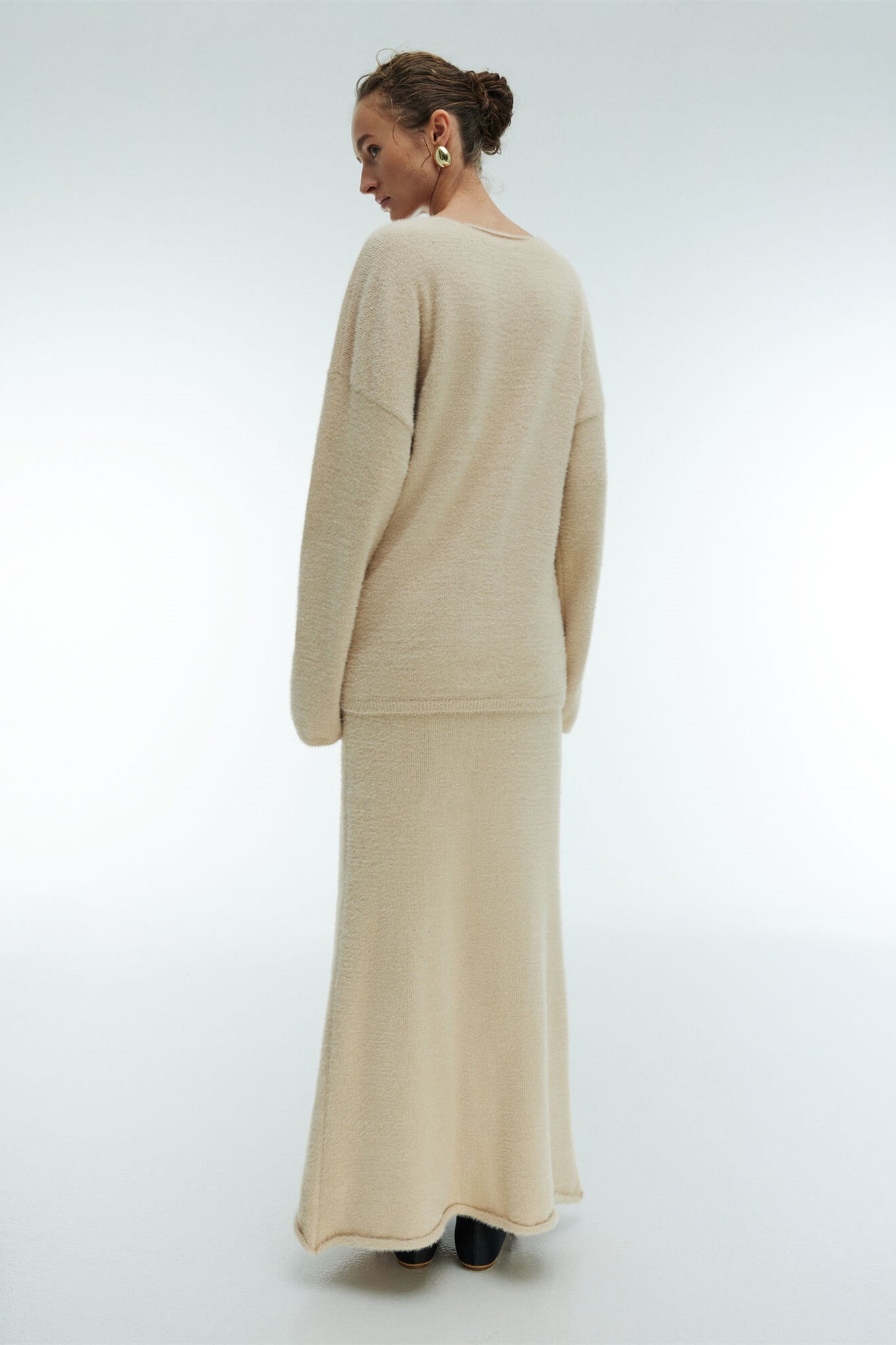 Woman in off-white boucle knit sweater and maxi skirt set with fuzzy slippers