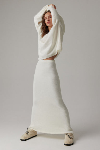 Woman in off-white boucle knit sweater and maxi skirt set with fuzzy slippers
