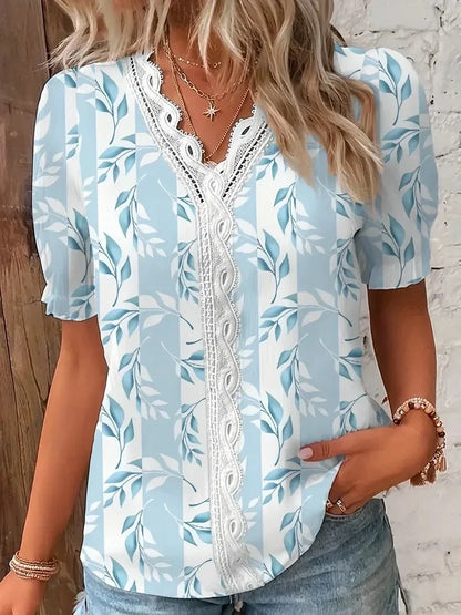 Light Blue - A woman wearing a light blue and white striped blouse with a blue botanical leaf print, featuring a white lace-trimmed V-neckline and short puff sleeves.