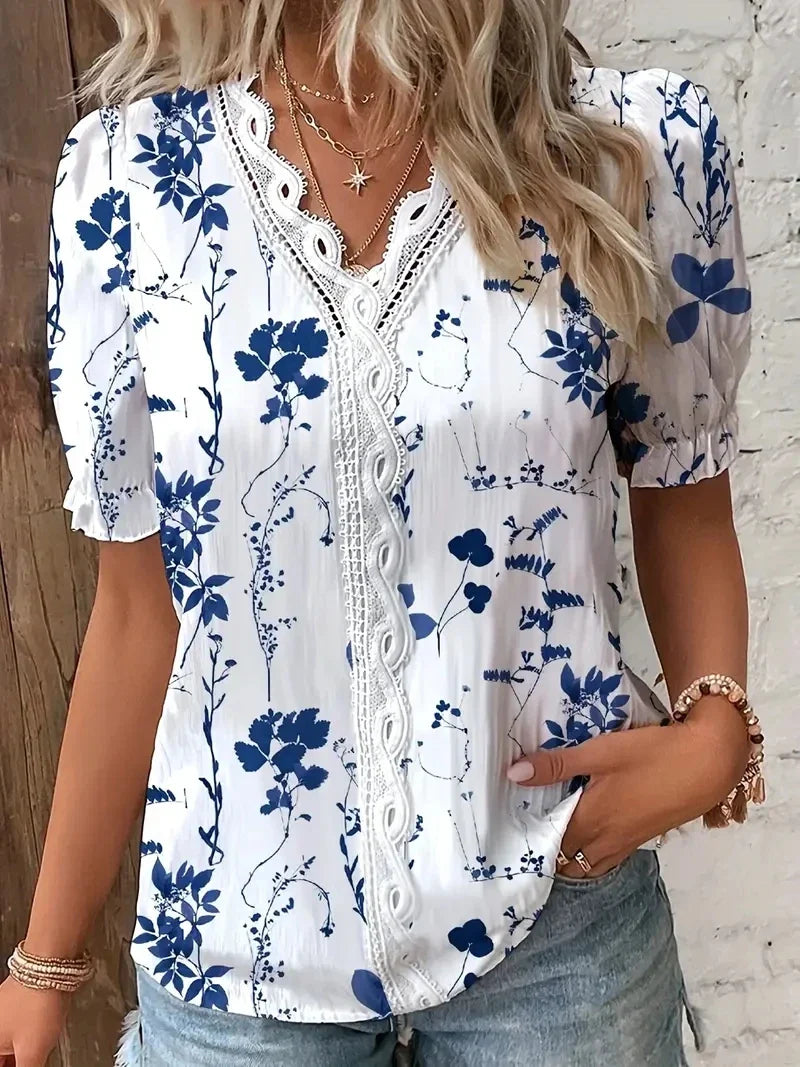 Dark Blue - A woman wearing a light blue and white striped blouse with a blue botanical leaf print, featuring a white lace-trimmed V-neckline and short puff sleeves.