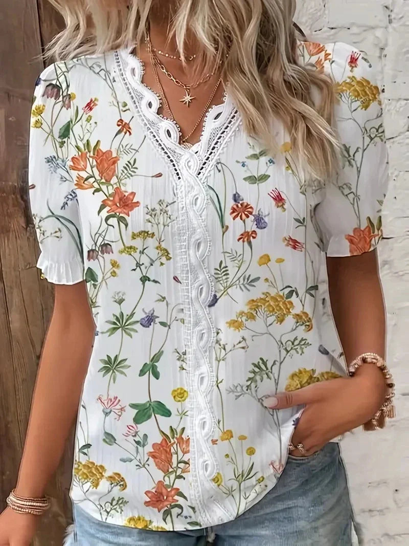 Beige - A woman wearing a light blue and white striped blouse with a blue botanical leaf print, featuring a white lace-trimmed V-neckline and short puff sleeves.
