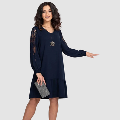 Dark Blue - A woman wearing a navy blue knee-length shift dress with long bishop sleeves featuring sheer lace panels, a V-neckline, and a ruffled flounce hem.