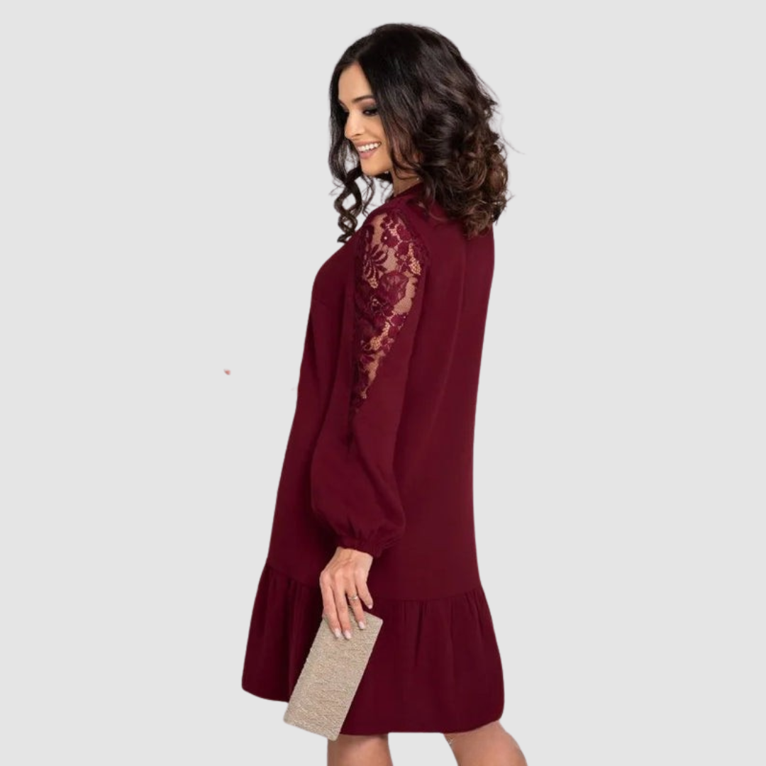 Burgundy - A woman wearing a navy blue knee-length shift dress with long bishop sleeves featuring sheer lace panels, a V-neckline, and a ruffled flounce hem.