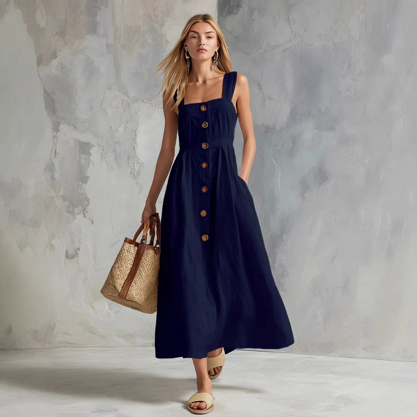 Navy - A woman modeling a chocolate brown linen-blend midi sundress with a square neckline, wide straps, and a button-down front, holding a woven straw tote bag.