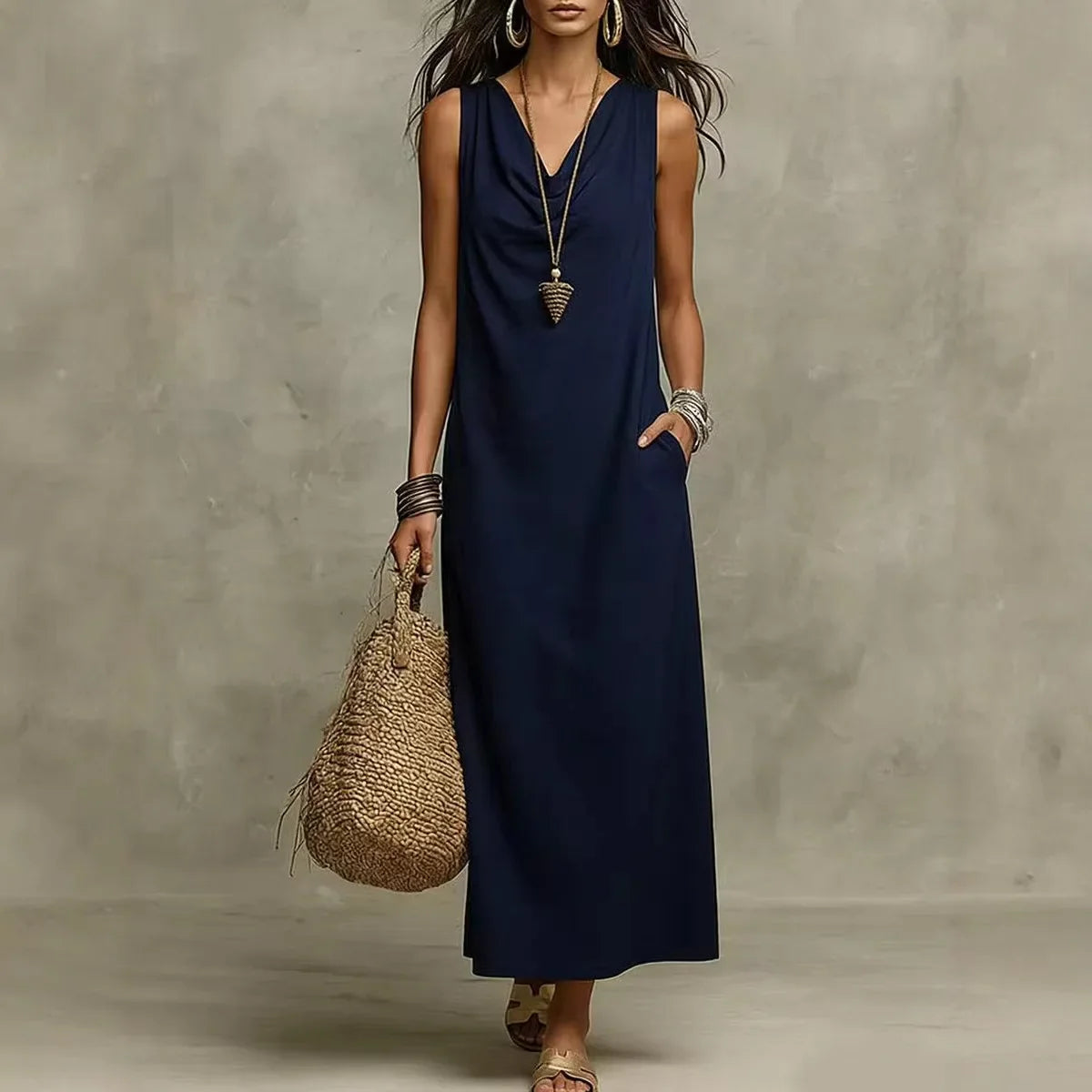 Navy Blue - A woman wearing a sleeveless, floor-length maxi sundress featuring a draped cowl neckline and side pockets, holding a woven straw tote bag