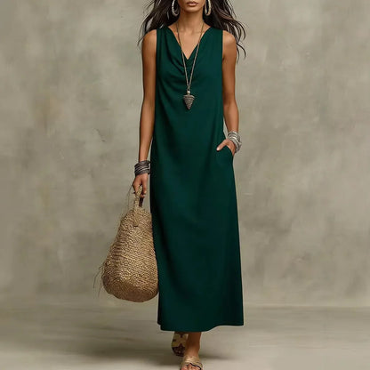 Dark Green - A woman wearing a sleeveless, floor-length maxi sundress featuring a draped cowl neckline and side pockets, holding a woven straw tote bag