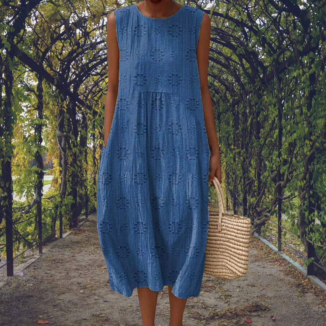Blue - Woman wearing a sleeveless, A-line midi sundress featuring an all-over 3D floral applique pattern and side seam pockets, standing on a gravel path.