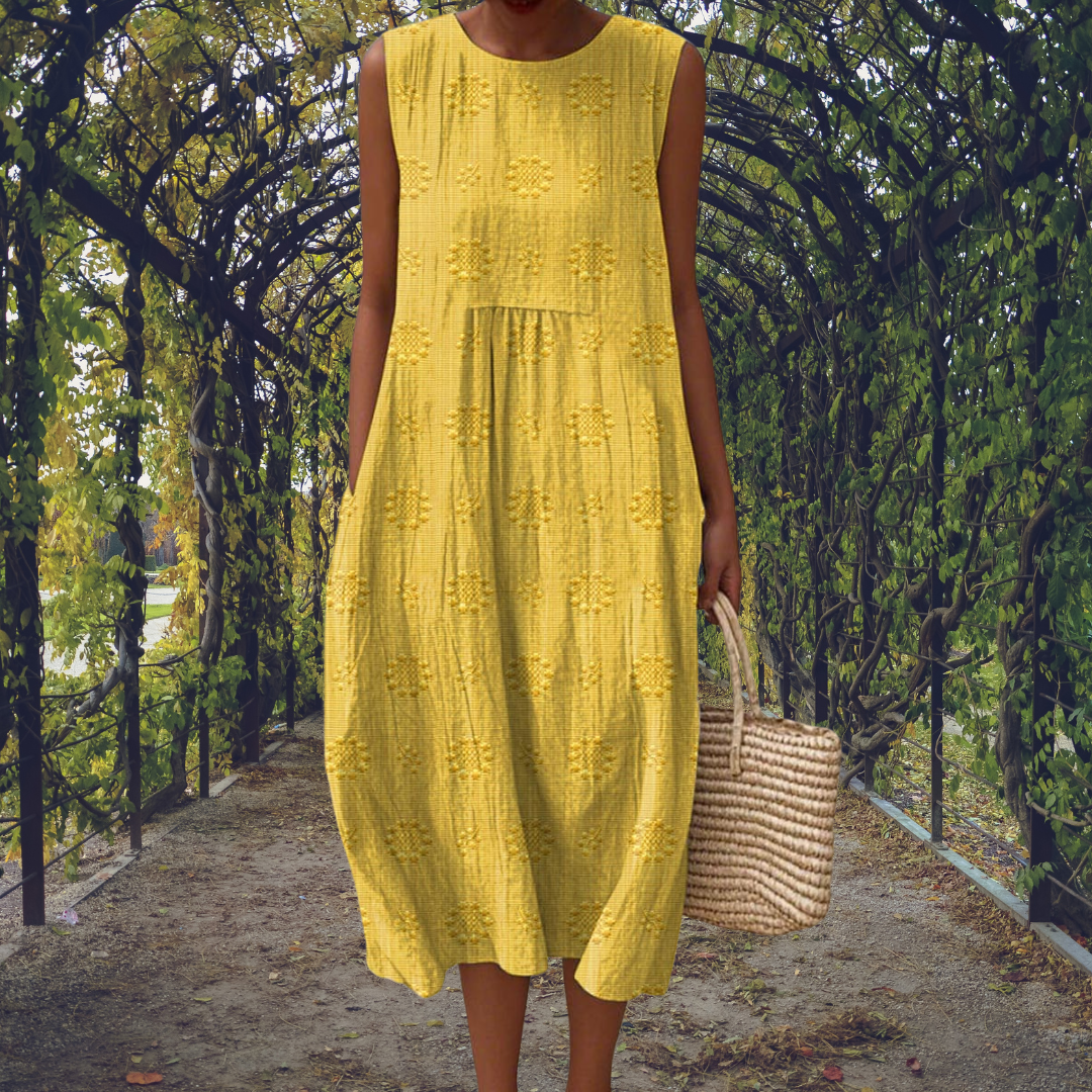 Yellow - Woman wearing a sleeveless, A-line midi sundress featuring an all-over 3D floral applique pattern and side seam pockets, standing on a gravel path.