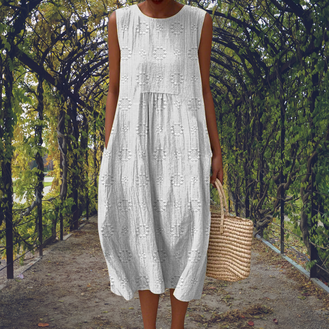 White - Woman wearing a sleeveless, A-line midi sundress featuring an all-over 3D floral applique pattern and side seam pockets, standing on a gravel path.