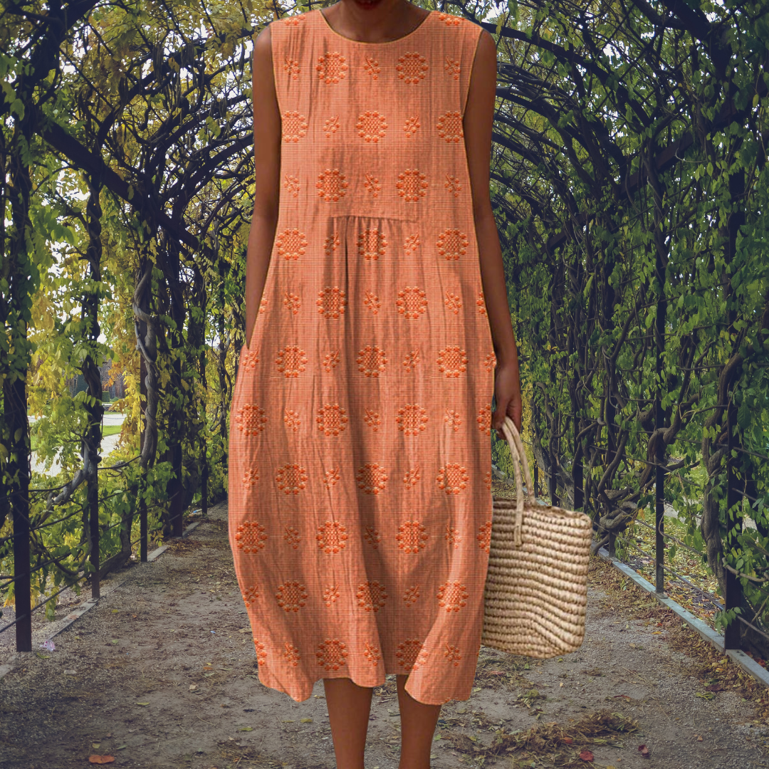 Orange - Woman wearing a sleeveless, A-line midi sundress featuring an all-over 3D floral applique pattern and side seam pockets, standing on a gravel path.