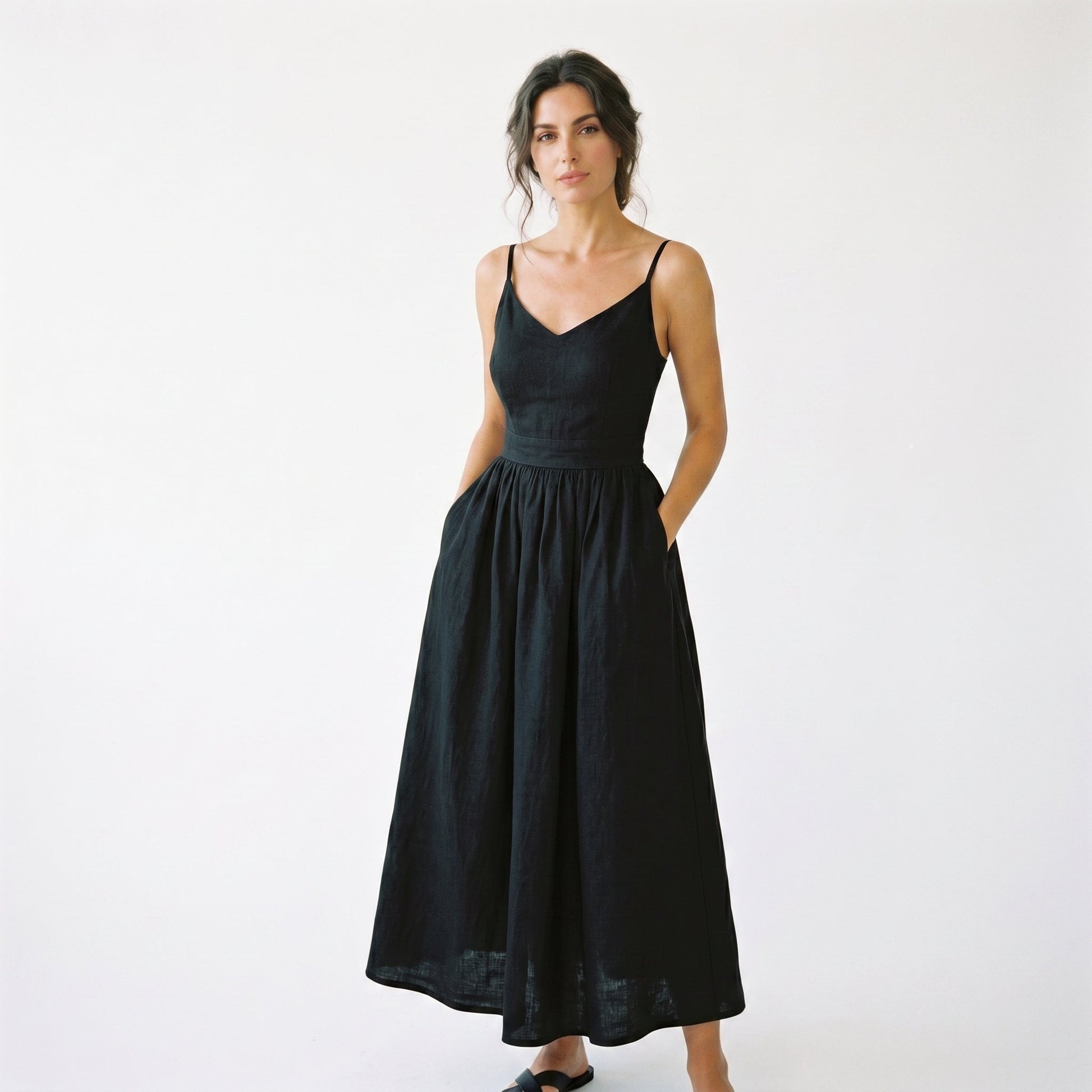 Black - Model wearing a solid woven maxi dress featuring tie-shoulder straps, a fitted waist, and a full sweeping skirt against a white studio background.