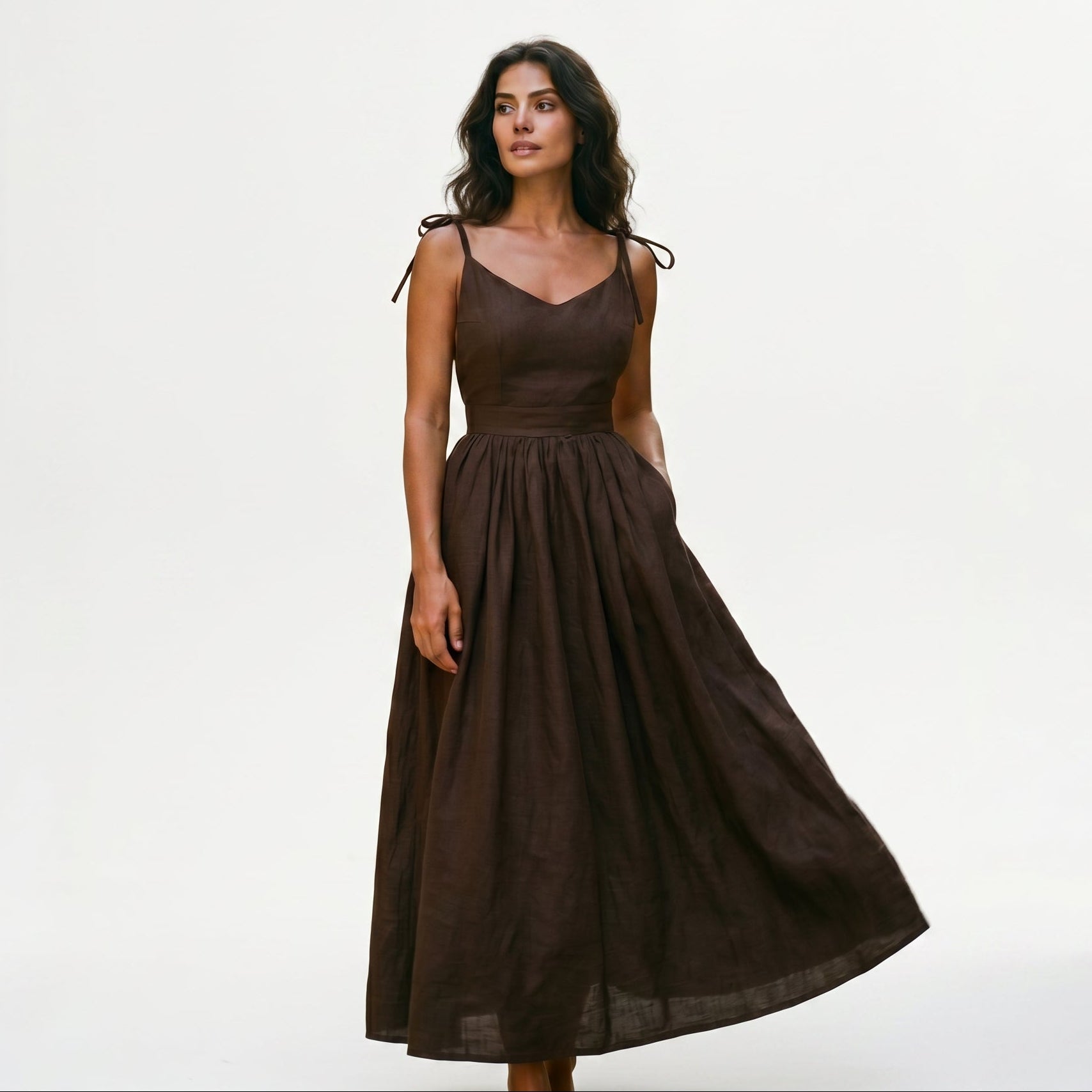 Brown - Model wearing a solid woven maxi dress featuring tie-shoulder straps, a fitted waist, and a full sweeping skirt against a white studio background.
