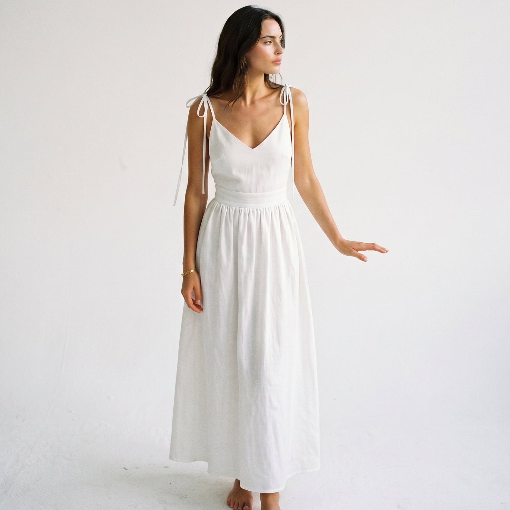 White - Model wearing a solid woven maxi dress featuring tie-shoulder straps, a fitted waist, and a full sweeping skirt against a white studio background.