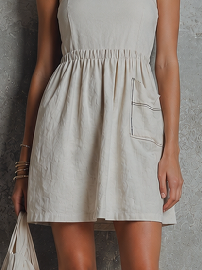 Off-White - Woman wearing a woven mini dress with spaghetti straps, a gathered elastic waist, and a front patch pocket with contrast stitching, holding a fabric bag.