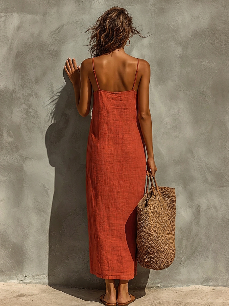 White - Woman wearing a textured, relaxed-fit spaghetti strap maxi dress, holding a large woven tote bag against a concrete wall.