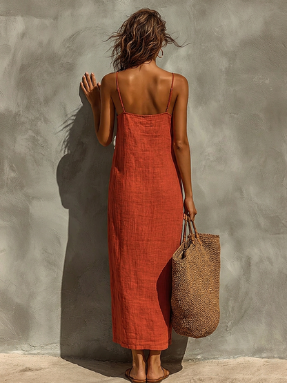 White - Woman wearing a textured, relaxed-fit spaghetti strap maxi dress, holding a large woven tote bag against a concrete wall.