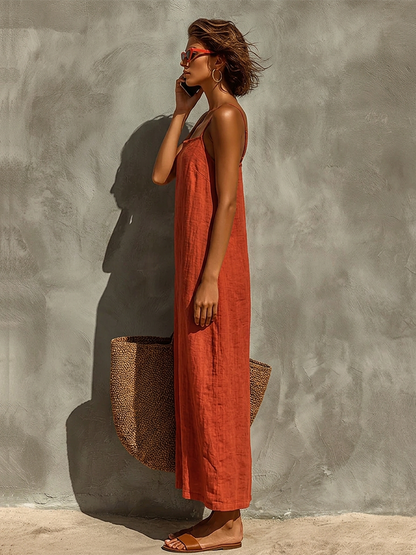 White - Woman wearing a textured, relaxed-fit spaghetti strap maxi dress, holding a large woven tote bag against a concrete wall.