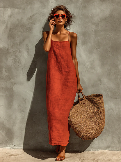 Red - Woman wearing a textured, relaxed-fit spaghetti strap maxi dress, holding a large woven tote bag against a concrete wall.