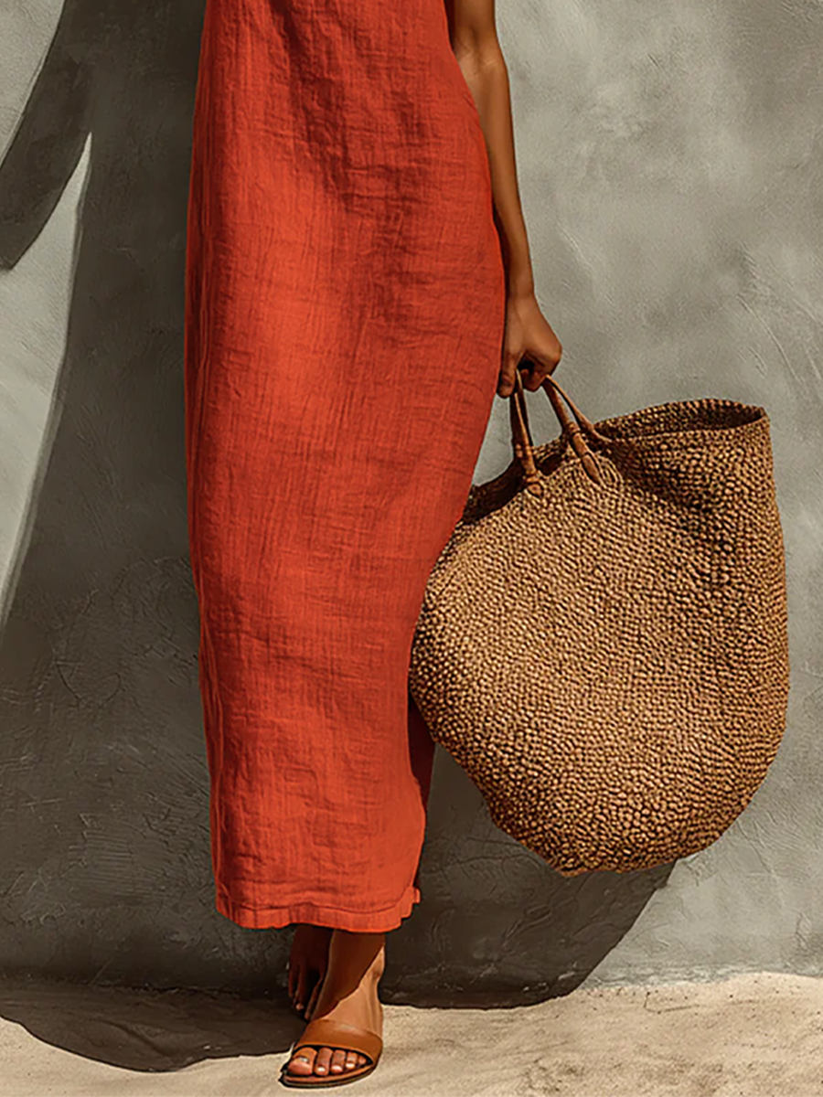 Red - Woman wearing a textured, relaxed-fit spaghetti strap maxi dress, holding a large woven tote bag against a concrete wall.