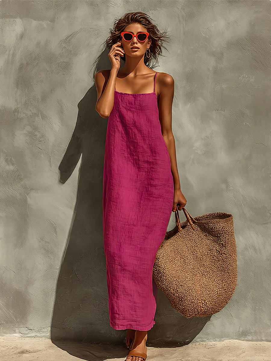 Purple - Woman wearing a textured, relaxed-fit spaghetti strap maxi dress, holding a large woven tote bag against a concrete wall.