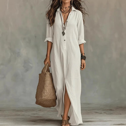 White - A woman wearing a relaxed-fit white linen maxi sundress with a collared V-neck, rolled sleeves, and a front slit, carrying a woven straw tote bag.