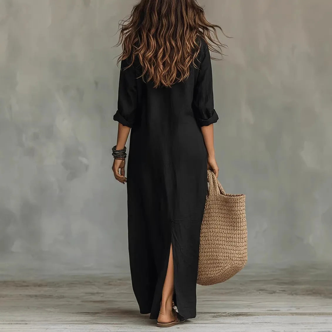Black - A woman wearing a relaxed-fit white linen maxi sundress with a collared V-neck, rolled sleeves, and a front slit, carrying a woven straw tote bag.