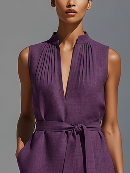 Purple - Woman walking outdoors wearing a sleeveless V-neck mini dress with shoulder pleating, a tie waist, and side pockets, carrying a woven tote bag.