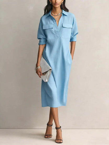 Blue - A woman wearing a light blue linen midi shirt dress with a collar, V-neckline, chest flap pockets, and half sleeves, styled with black strappy heels and a striped clutch.