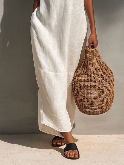 Woman modeling a sleeveless relaxed maxi dress featuring a textured V-neckline and fluid drape, carrying a large woven basket bag.