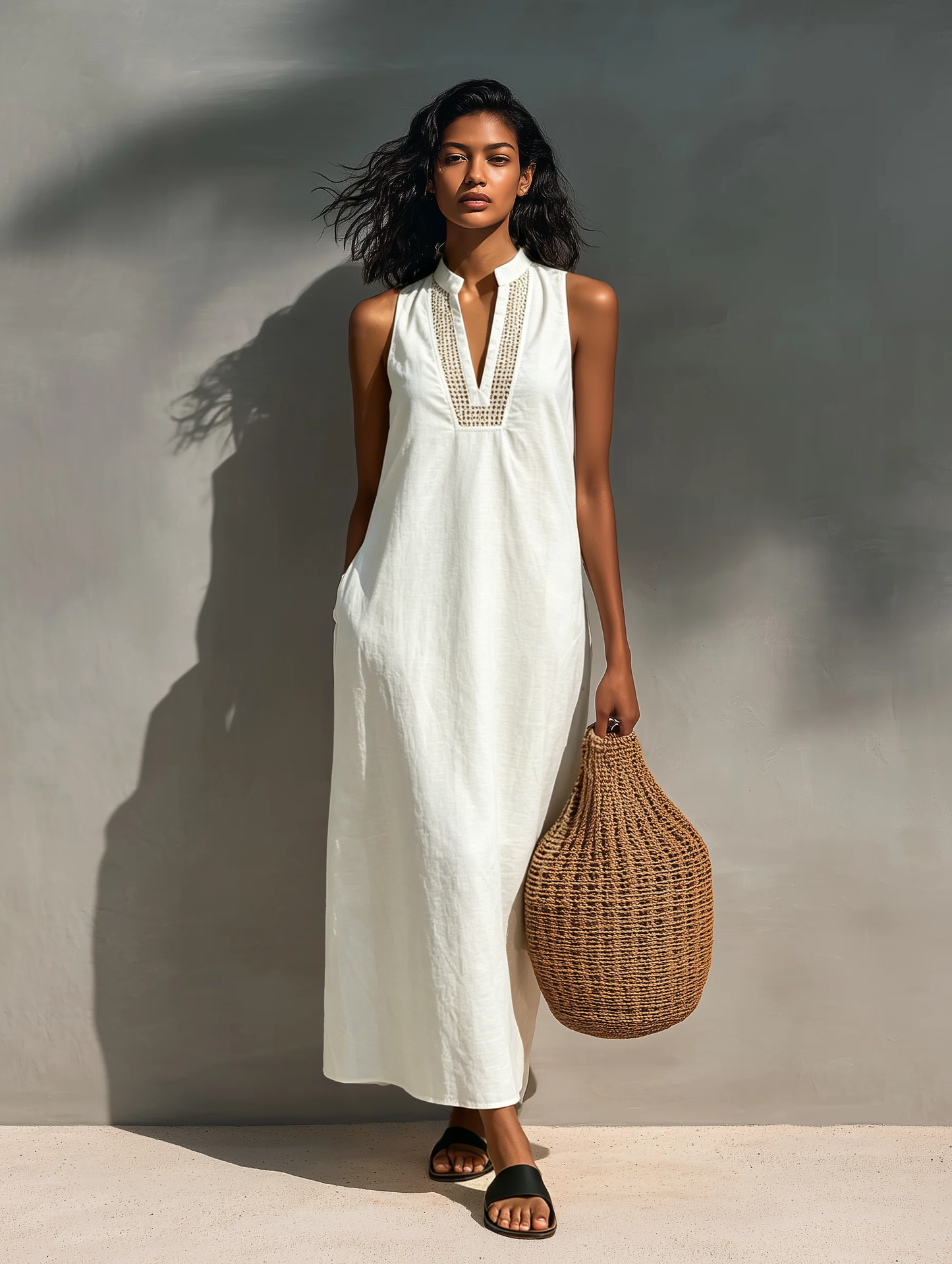 Woman modeling a sleeveless relaxed maxi dress featuring a textured V-neckline and fluid drape, carrying a large woven basket bag.
