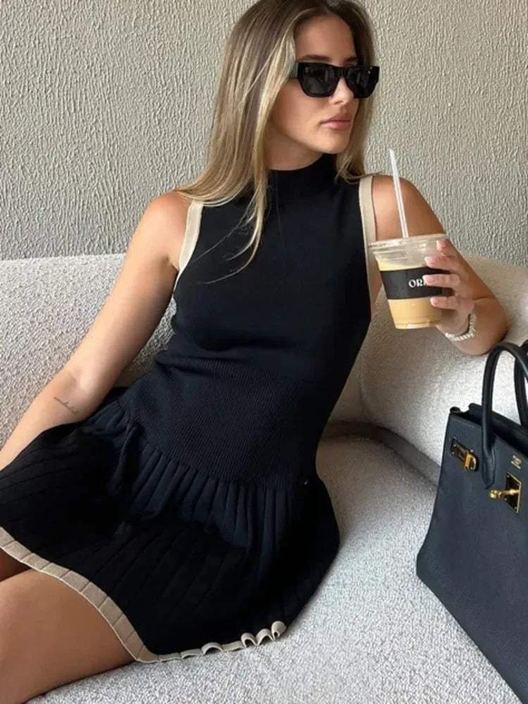 Woman in black ribbed knit mini dress with tan trim, holding coffee and purse.