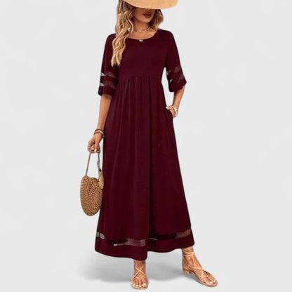 Red - A woman wearing a burgundy maxi dress with elbow-length sleeves and a scoop neckline, featuring sheer mesh stripe inserts on the sleeves and hem, styled with a straw hat and bag.