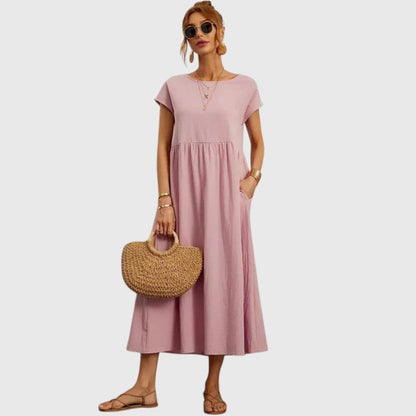 Rose - A woman wearing a navy blue, cap-sleeve midi sundress with an empire waist and side pockets, styled with a woven straw handbag and flat sandals.