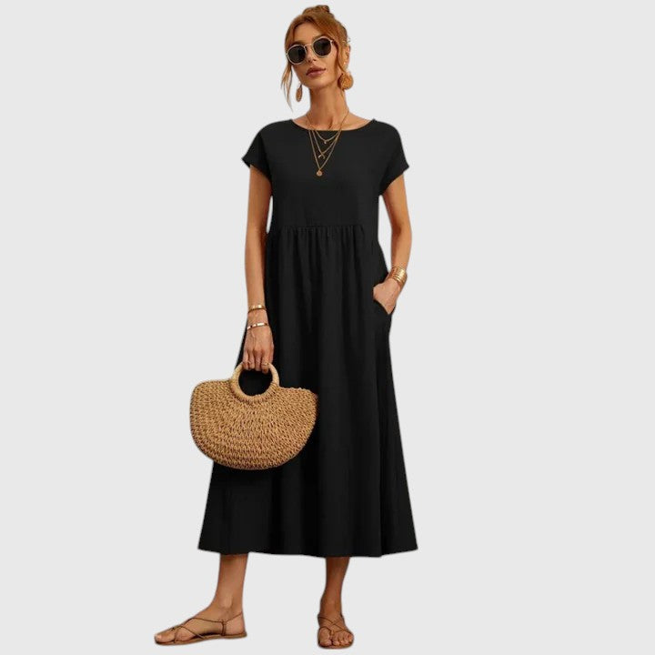 Black - A woman wearing a navy blue, cap-sleeve midi sundress with an empire waist and side pockets, styled with a woven straw handbag and flat sandals.