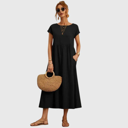 Black - A woman wearing a navy blue, cap-sleeve midi sundress with an empire waist and side pockets, styled with a woven straw handbag and flat sandals.
