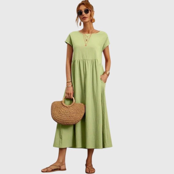 Light Green - A woman wearing a navy blue, cap-sleeve midi sundress with an empire waist and side pockets, styled with a woven straw handbag and flat sandals.