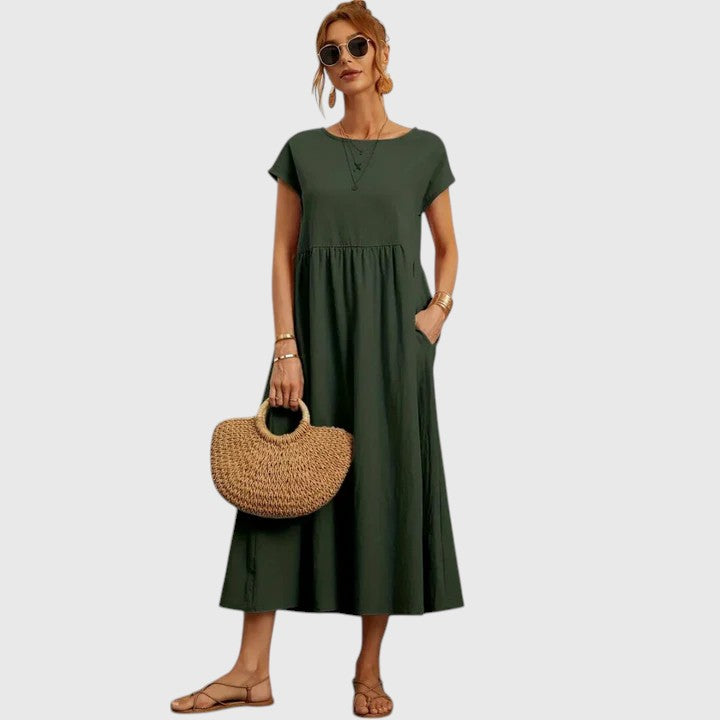Dark Green - A woman wearing a navy blue, cap-sleeve midi sundress with an empire waist and side pockets, styled with a woven straw handbag and flat sandals.