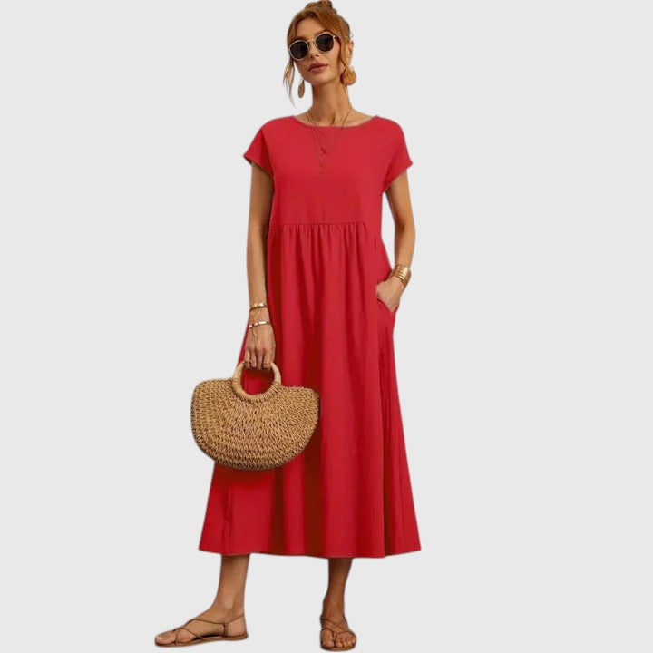 Red - A woman wearing a navy blue, cap-sleeve midi sundress with an empire waist and side pockets, styled with a woven straw handbag and flat sandals.