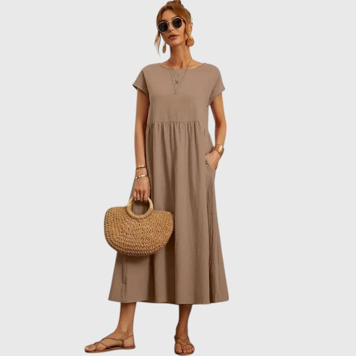 Khaki - A woman wearing a navy blue, cap-sleeve midi sundress with an empire waist and side pockets, styled with a woven straw handbag and flat sandals.