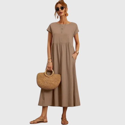 Khaki - A woman wearing a navy blue, cap-sleeve midi sundress with an empire waist and side pockets, styled with a woven straw handbag and flat sandals.